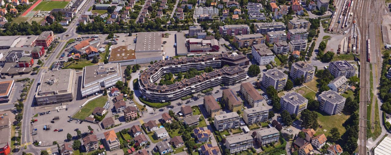 Texturiertes 3D-Mesh eines Wohnquartiers mit geschwungener Wohnüberbauung, Gewerbebauten und Gleisfeld