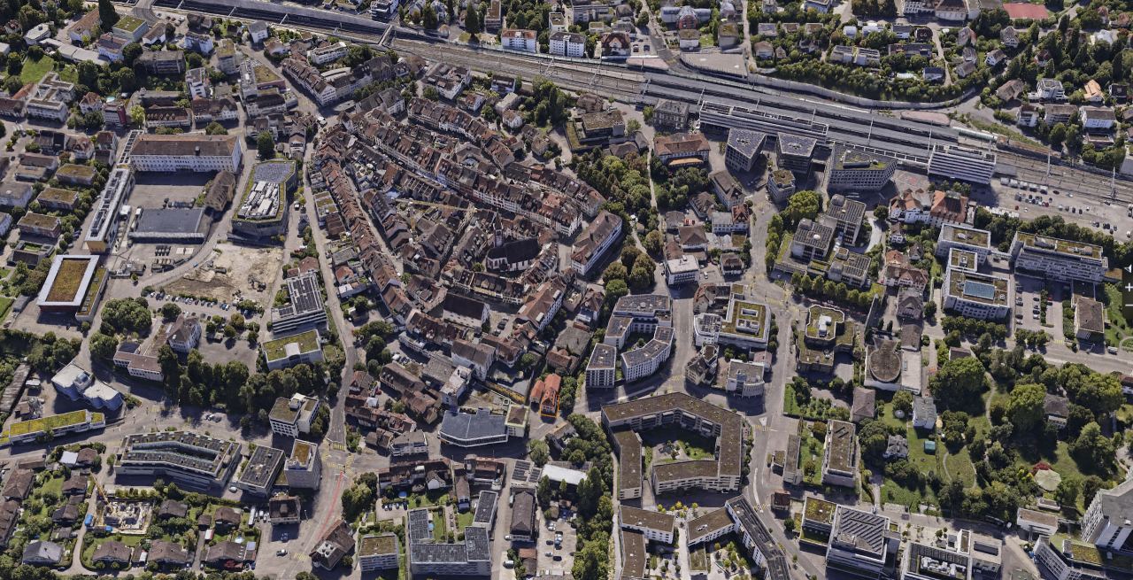 Gaussian splat of a small town from a greater height, with densely built quarters, streets and a track field in the background