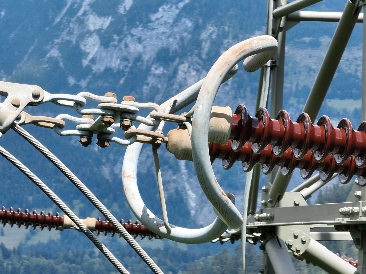 Drohnen-Inspektionsaufnahme einer Hochspannungsleitung, Isolatoren und Abspannklemmen im Detail vor Bergkulisse