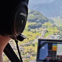 Martin Clement wearing a headset in the helicopter above the valley, mission planning running on the tablet