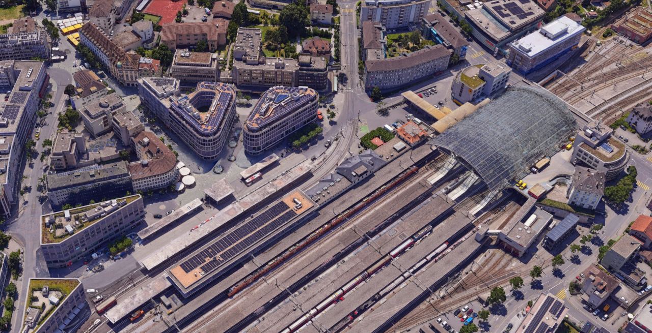 Texturiertes 3D-Mesh des Bahnhofs Chur aus dem Schrägblick, mit Gleisfeld, gewölbter Glashalle und den umliegenden Geschäftshäusern
