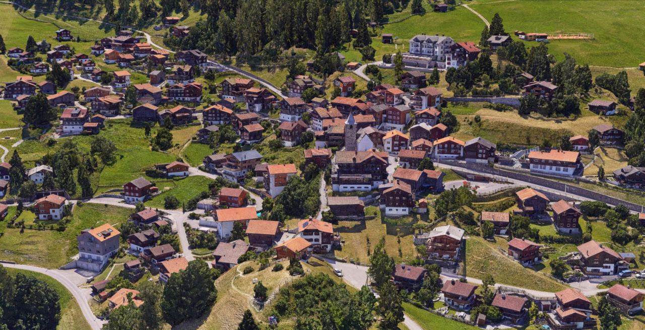 Texturiertes 3D-Mesh eines Bergdorfs mit Holzhäusern, Kirchturm, Wiesen und Wald